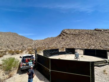 Desert setup with black barriers and two men near a truck under a clear blue sky.