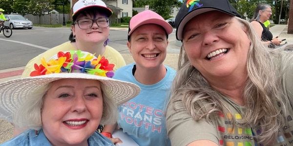Four smiling women outdoors, showing pride and support with colorful accessories.