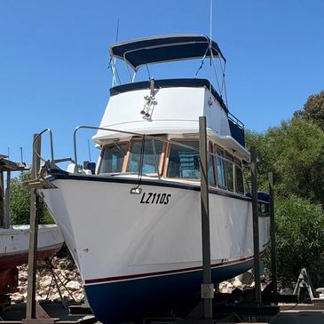 White and blue boat docked on dry land under a clear blue sky.