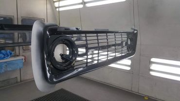 Freshly painted black car grille hanging in a workshop.