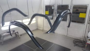 Glossy black automotive parts hanging to dry in a spray booth.