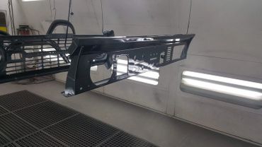 Glossy black car bumpers hanging in a paint booth.