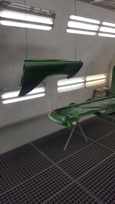 Green car parts hanging and drying in a paint booth.