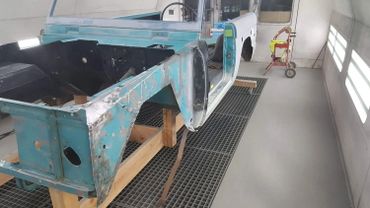 Partially restored vintage vehicle body in a workshop with wooden supports.