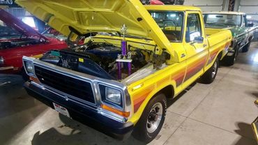 Yellow vintage pickup truck with hood open and trophy inside at a car show.
