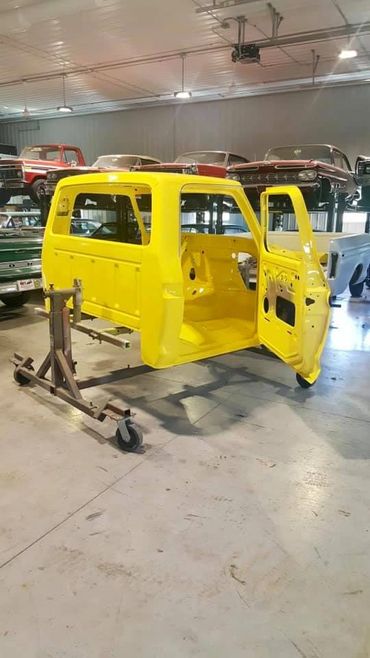 Bright yellow vehicle body shell in a workshop surrounded by classic cars.