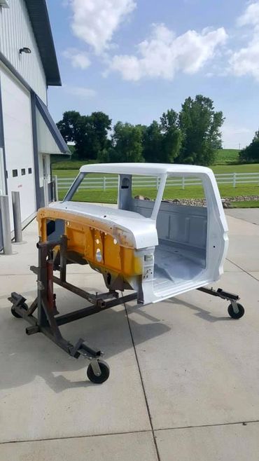 Vehicle cabin shell mounted on a metal frame outdoors near a building.