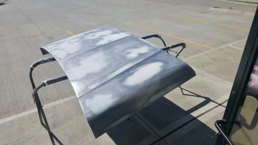 A car hood primed and ready for painting, resting on a stand outdoors.
