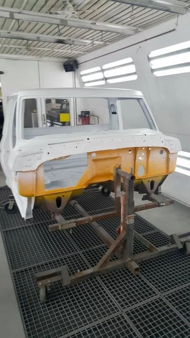 Vehicle body frame partially painted inside a workshop.