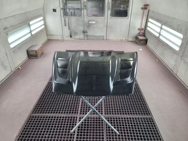 Glossy black car hood with vents in a spray booth.