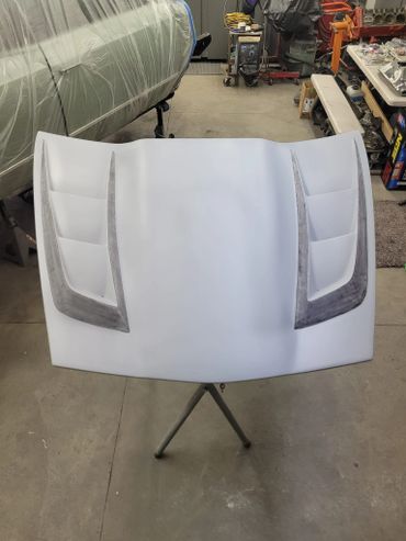 A primed car hood with vent details in a workshop.