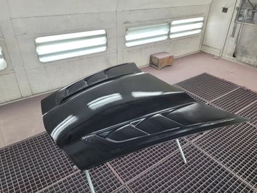A glossy black car hood with vents in a paint booth.