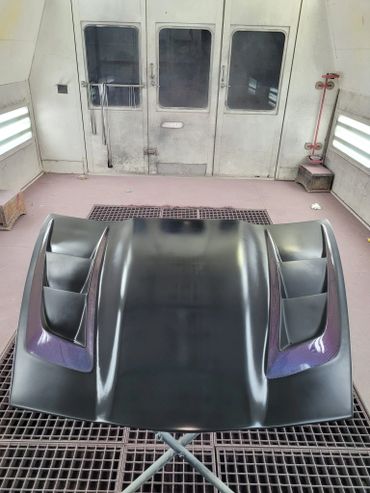 Glossy black car hood with aerodynamic vents in a workshop.
