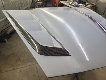 Close-up of a sleek white car hood with carbon fiber vents.