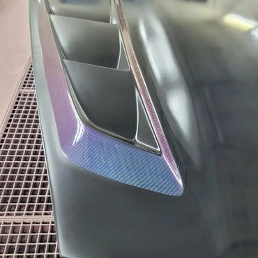 Close-up of a car hood vent with a glossy, gradient-colored carbon fiber trim.