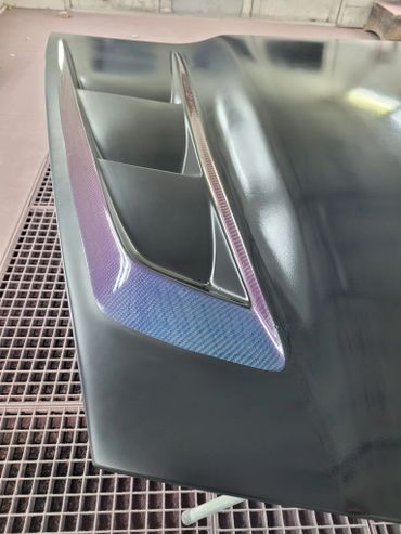 Close-up of a black car hood with carbon fiber vents.