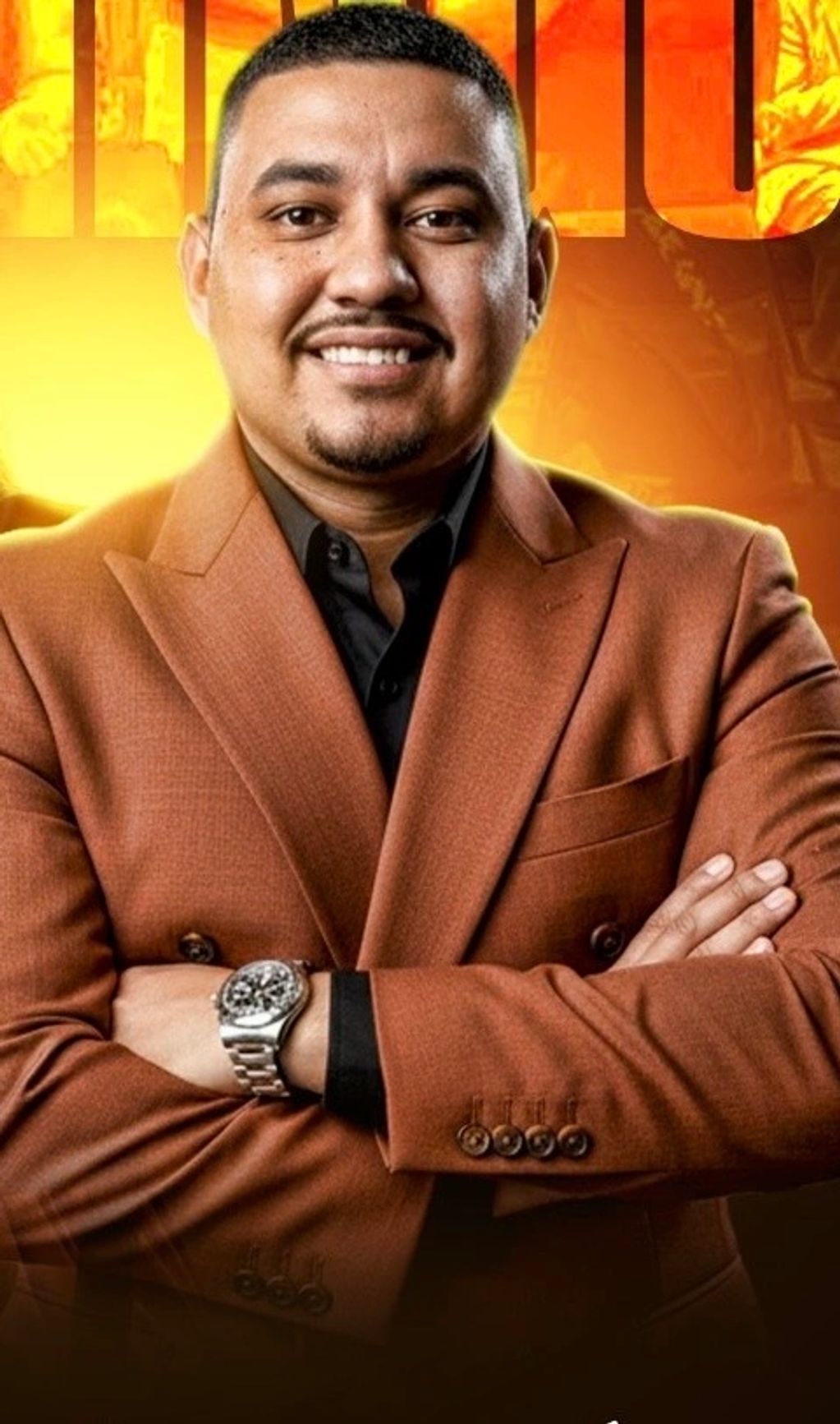 Confident man in a brown blazer smiling with arms crossed.