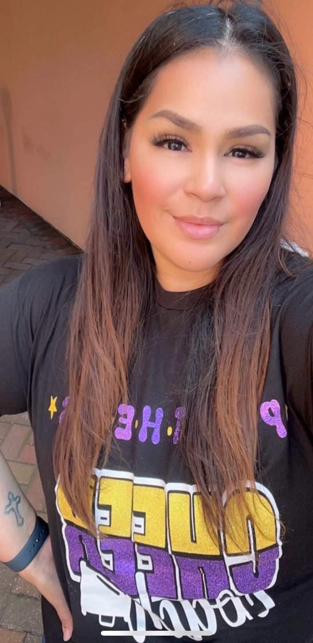 Smiling woman with long hair wearing a colorful graphic t-shirt and a wristband.