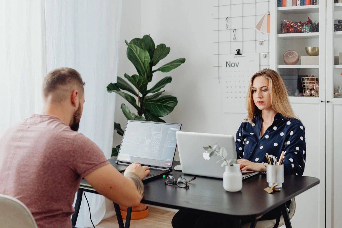 Two people working on laptops at a black table in a modern office.