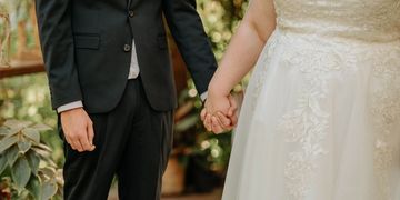 A bride and groom holding hands, dressed in wedding attire.
