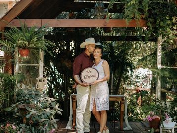 Couple holding a 'We Eloped' sign in a garden setting.