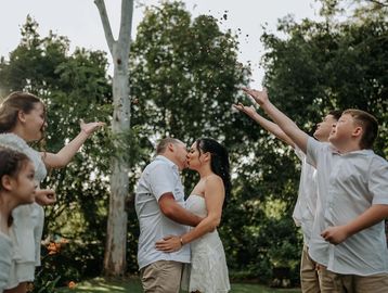 Couple kissing outdoors surrounded by family in a joyful moment.