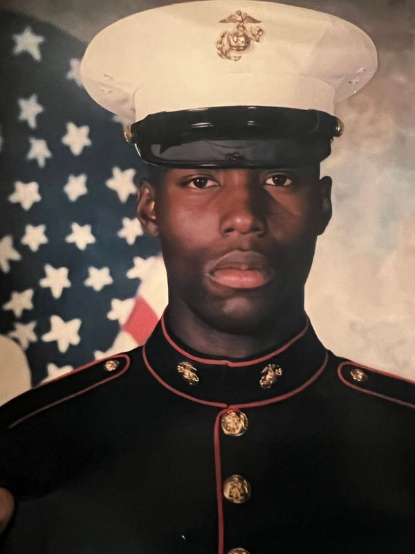 Portrait of a Marine in full dress uniform with an American flag backdrop.