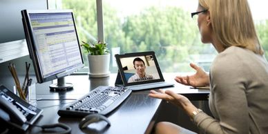 Woman video conferencing on tablet while working at desk with computer.