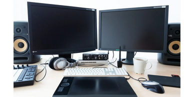 A dual-monitor computer setup with audio equipment and a graphics tablet on a desk.