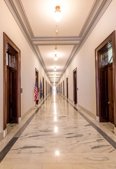 Long marble hallway with multiple doors and flags.