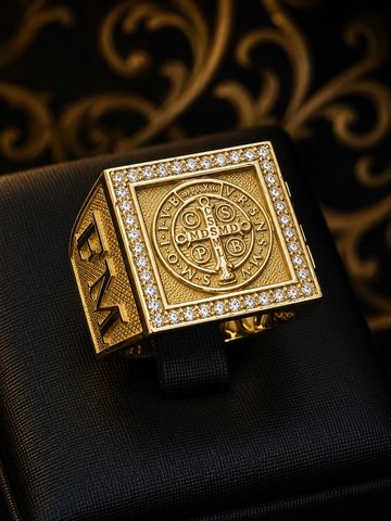 Anel dourado quadrado com pedras e inscrições detalhadas.