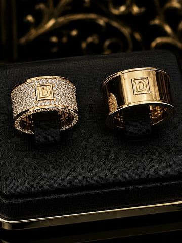 Two luxurious gold rings with a "D" emblem displayed on a black velvet box.