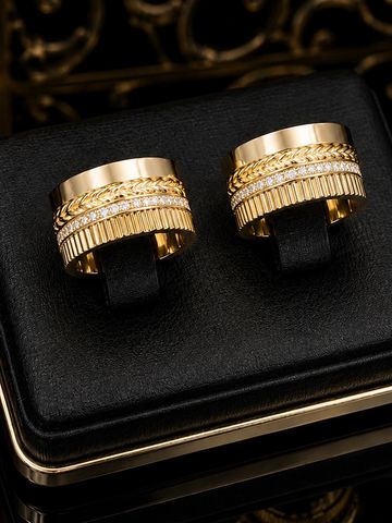 Elegant gold rings with intricate designs and embedded diamonds on a black cushion.