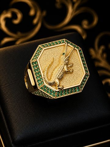 Anel dourado com design de lagarto e pedras verdes.