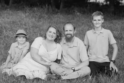 A family of four smiling and sitting on grass outdoors.