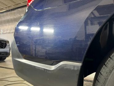 Close-up of a blue car's rear bumper with visible scratches and scuff marks.