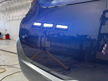 Close-up of a blue car's rear bumper with reflections of workshop lights.
