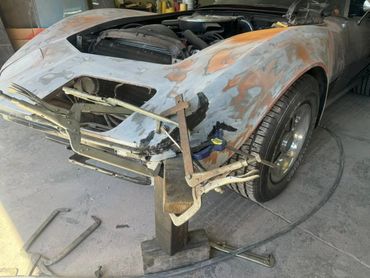 A vintage car undergoing bodywork repairs with clamps holding the front section.