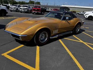 A classic gold Chevrolet Corvette parked in a lot with yellow lines.