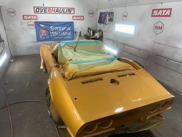 A yellow car in a paint shop, partially covered for painting.