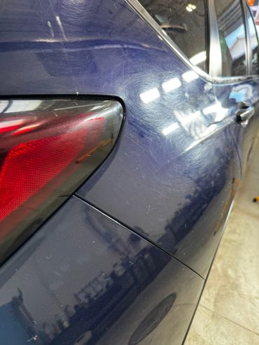 Close-up of a scratched dark blue car near the tail light.
