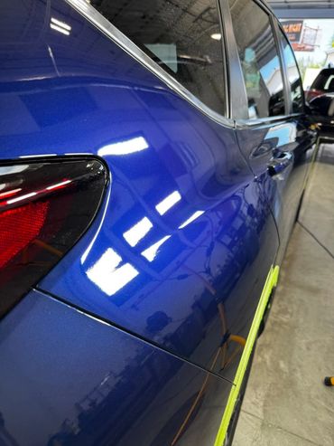 Close-up of a shiny blue car's rear side with reflections in a garage.