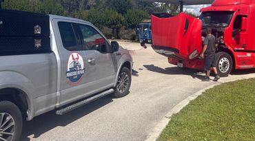 Roadside repair truck attending to a broken-down red semi-truck.