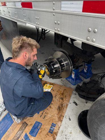 A mechanic in blue coveralls working on a truck brake assembly.