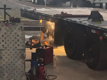 A worker welding underneath a flatbed trailer with sparks flying.