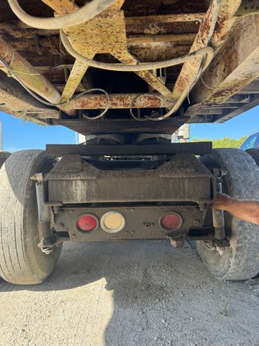 Underside of a rusty, dirty trailer with large rear tires and a person's arm visible.