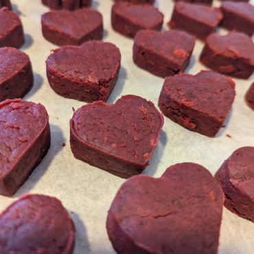Heart-shaped red velvet cookie dough on baking paper.