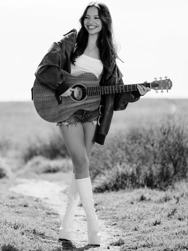 Smiling woman playing guitar outdoors in vintage style.