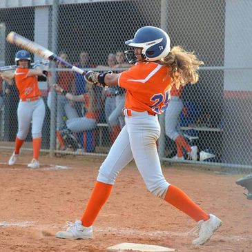 Girl in orange baseball uniform hitting a ball.