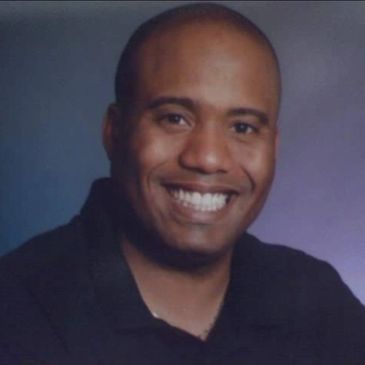 Smiling man with a bald head and dark shirt.